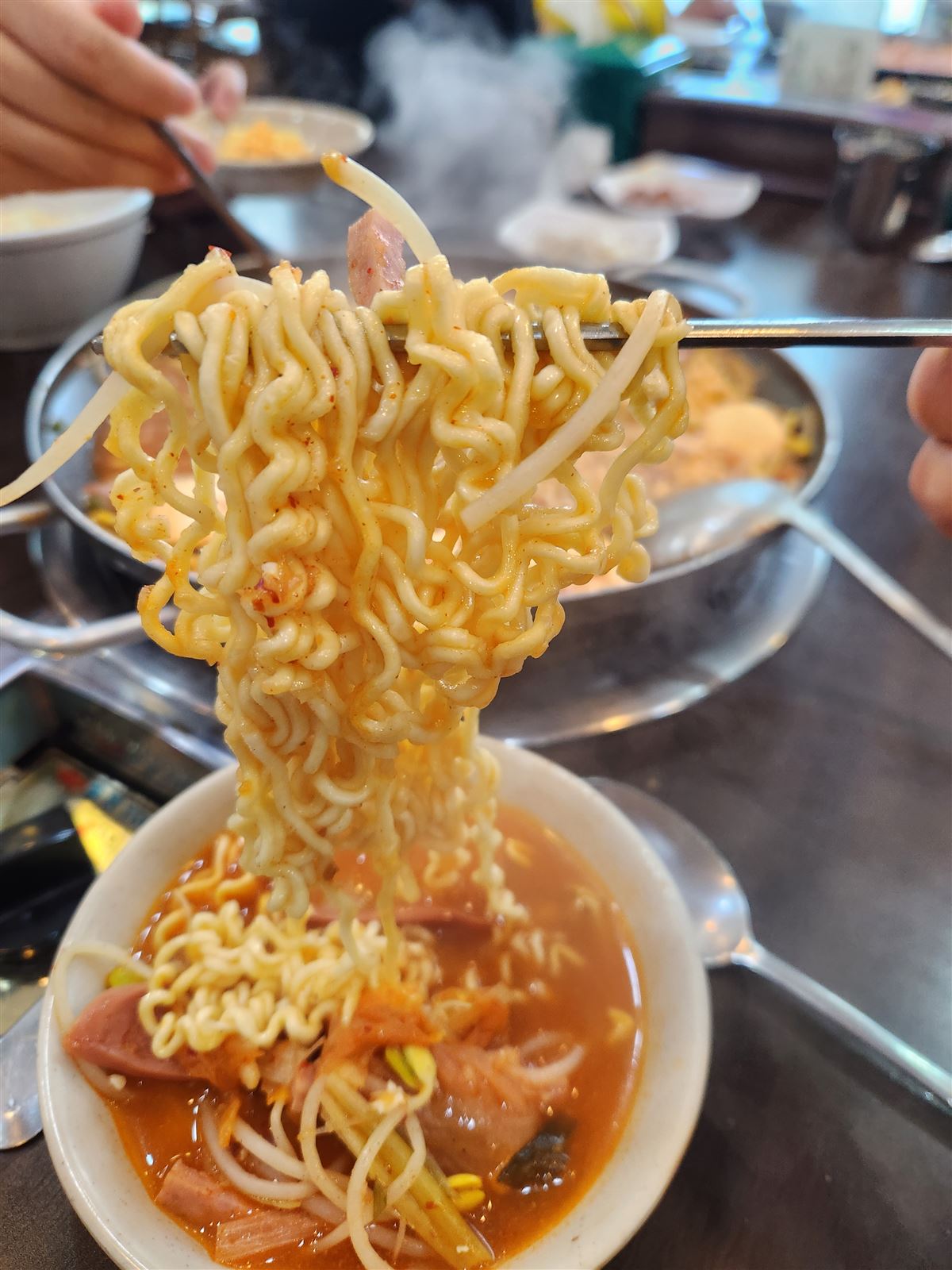 Lifting ramen noodles from budae jjigae broth — free refill at Songtan Budae Jjigae Myeongdong