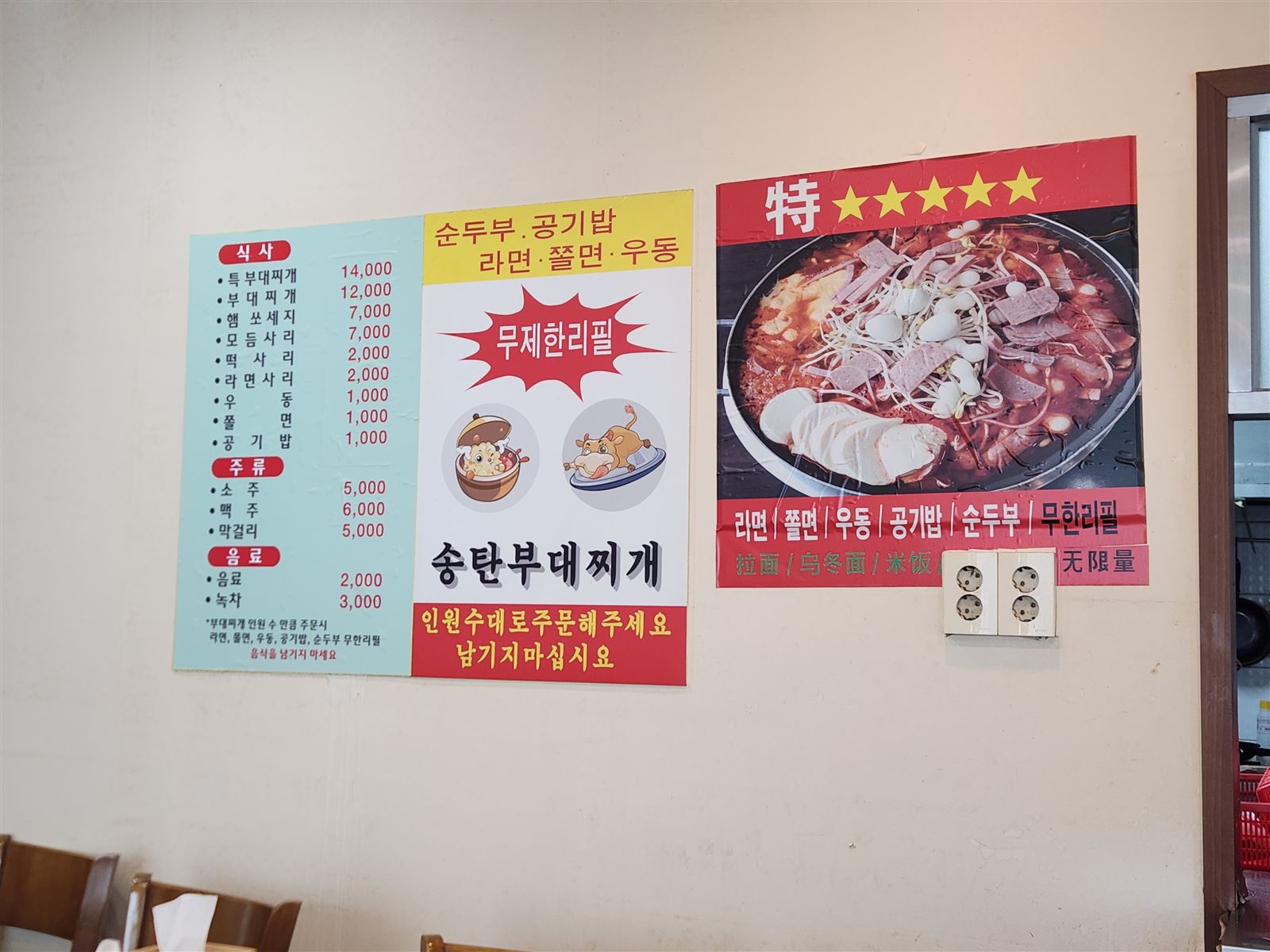 Wall poster listing free unlimited refills of ramen, jjolmyeon, udon, rice and tofu at Songtan Budae Jjigae Myeongdong