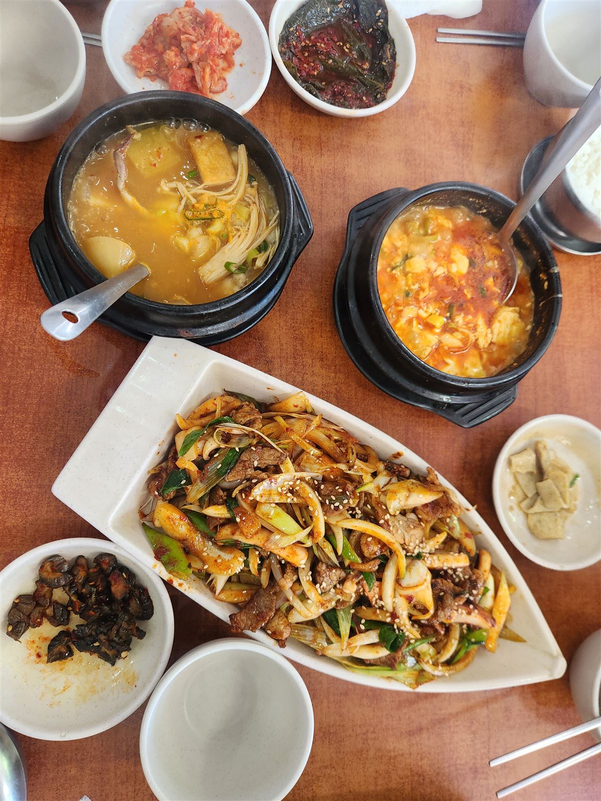 Full table spread with two stews, a stir-fry platter and banchan at Sogongdong Ttukbaegijip Seoul