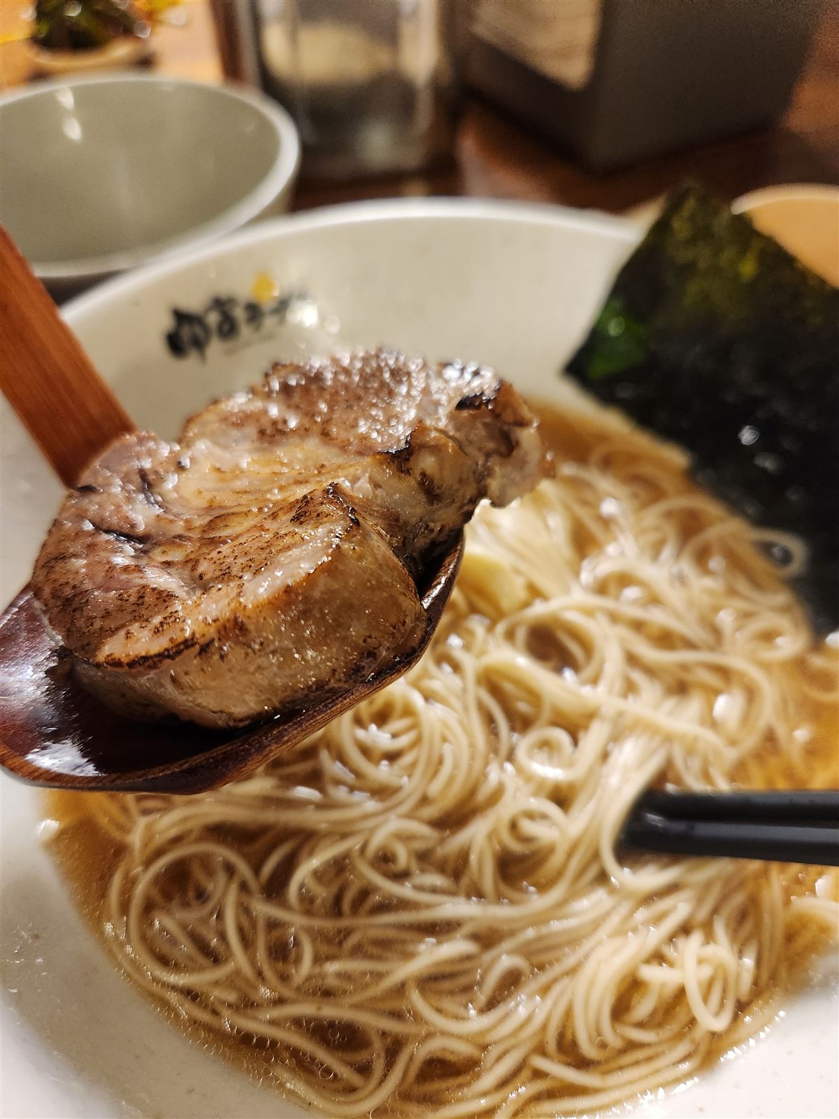 Flame-grilled chashu pork with smoky char on a wooden spoon over ramen noodles at Yuzu Ramen Seoul