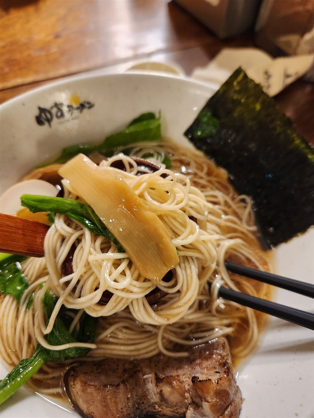 Thin ramen noodles lifted from a clear yuzu broth with menma bamboo and greens at Yuzu Ramen Seoul